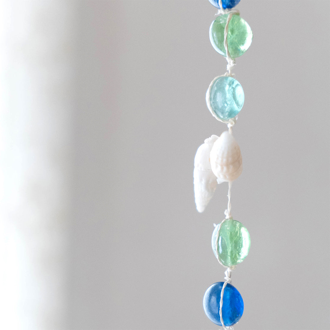 ブルーとグリーンのガラスとスターフィッシュのサンキャッチャーが窓辺で光を受けて揺れるマリンインテリア